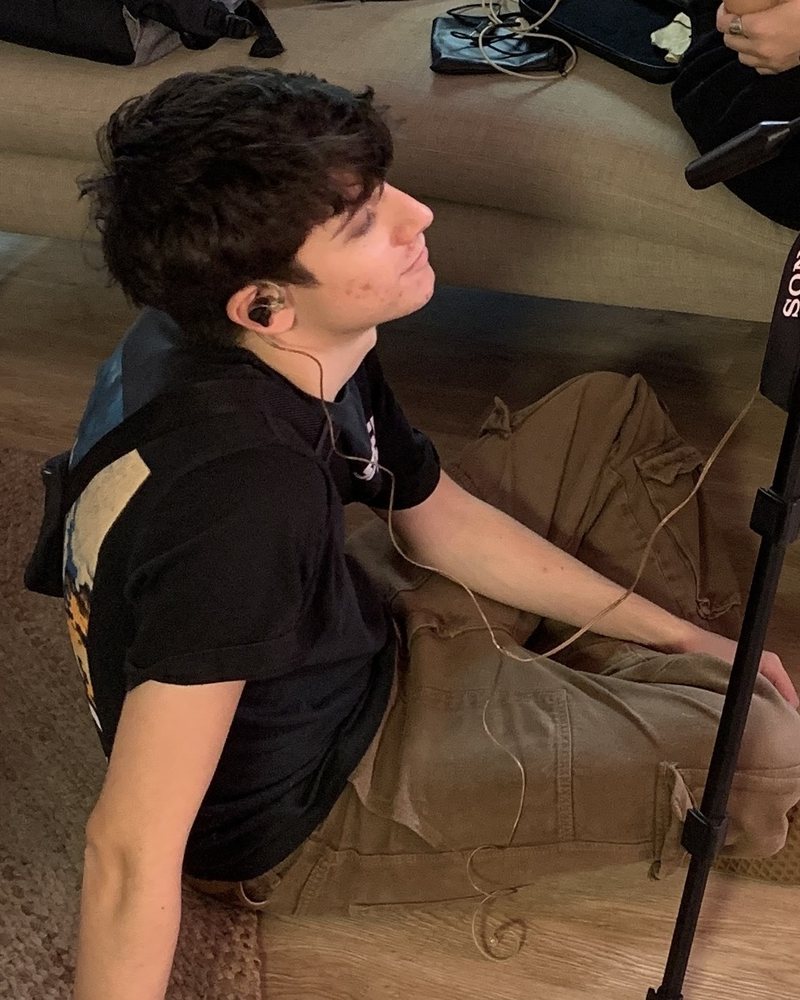 Ami, videographer, sitting on the floor on a shoot with earbuds in, listening